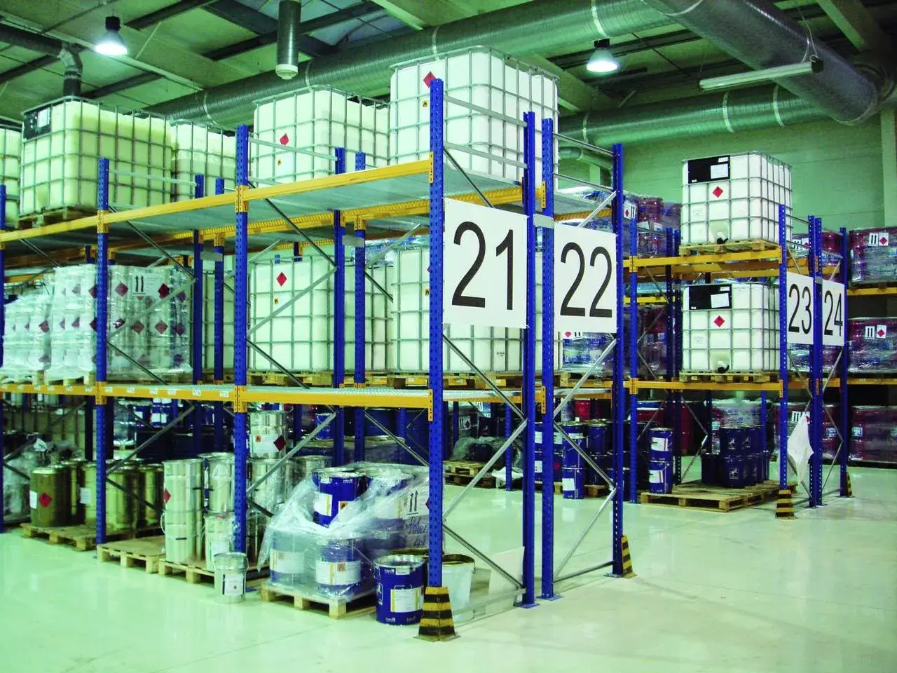 Plan hali produkcyjnej: regały z białymi i niebieskimi beczkami oraz dużymi zbiornikami IBC. Numery 21, 22, 23, 24 wskazują lokalizację.