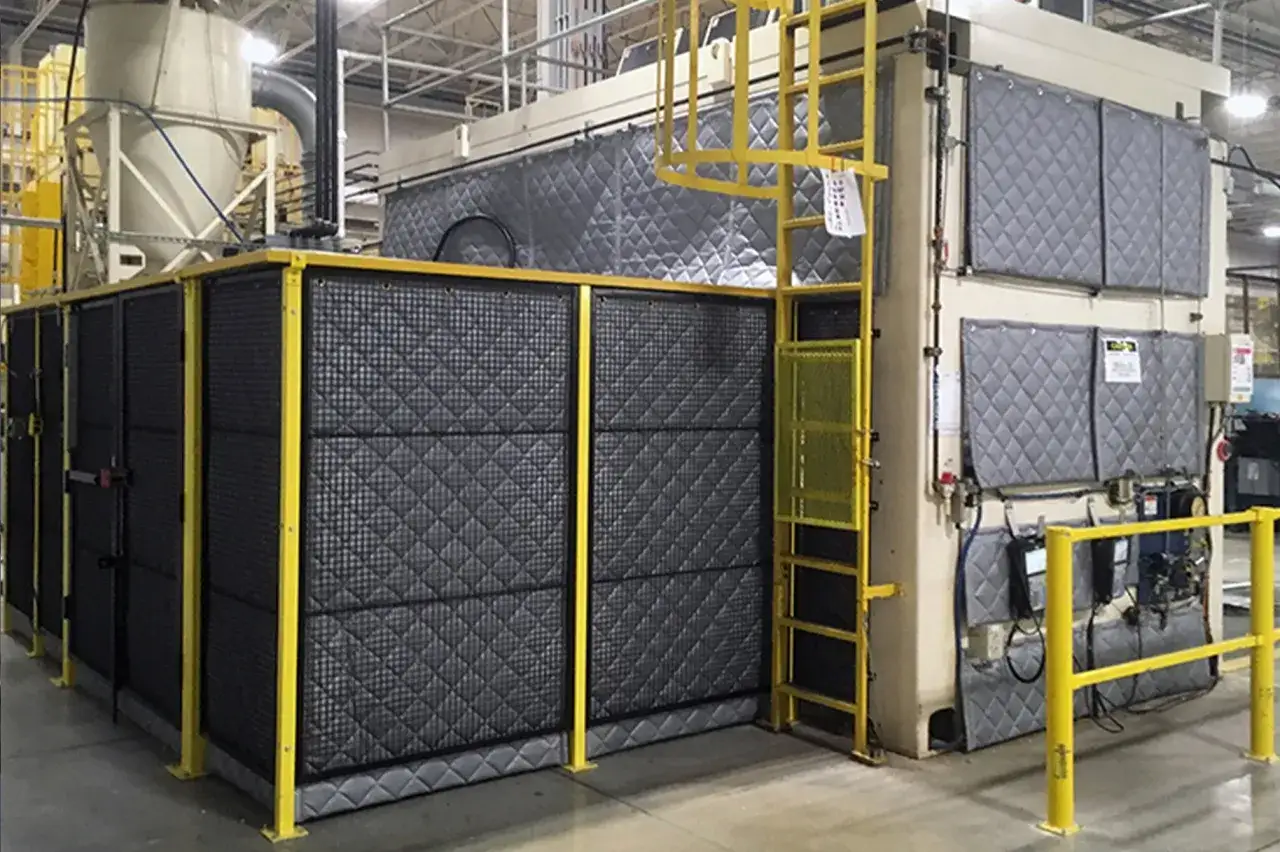 Máquina industrial con aislamiento acústico para controlar el nivel de presión sonora. Estructura metálica amarilla y paneles acolchados grises.