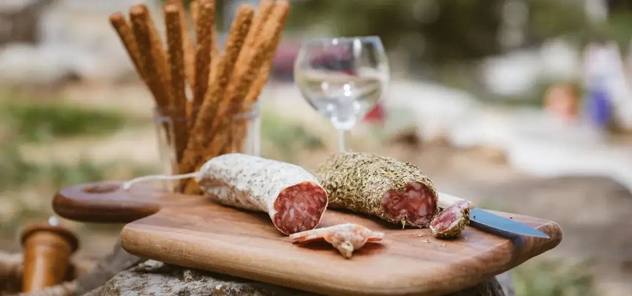 Deux saucissons, un nature et un aux herbes, sur une planche en bois. Idéal pour une recette saucisson simple et savoureuse.