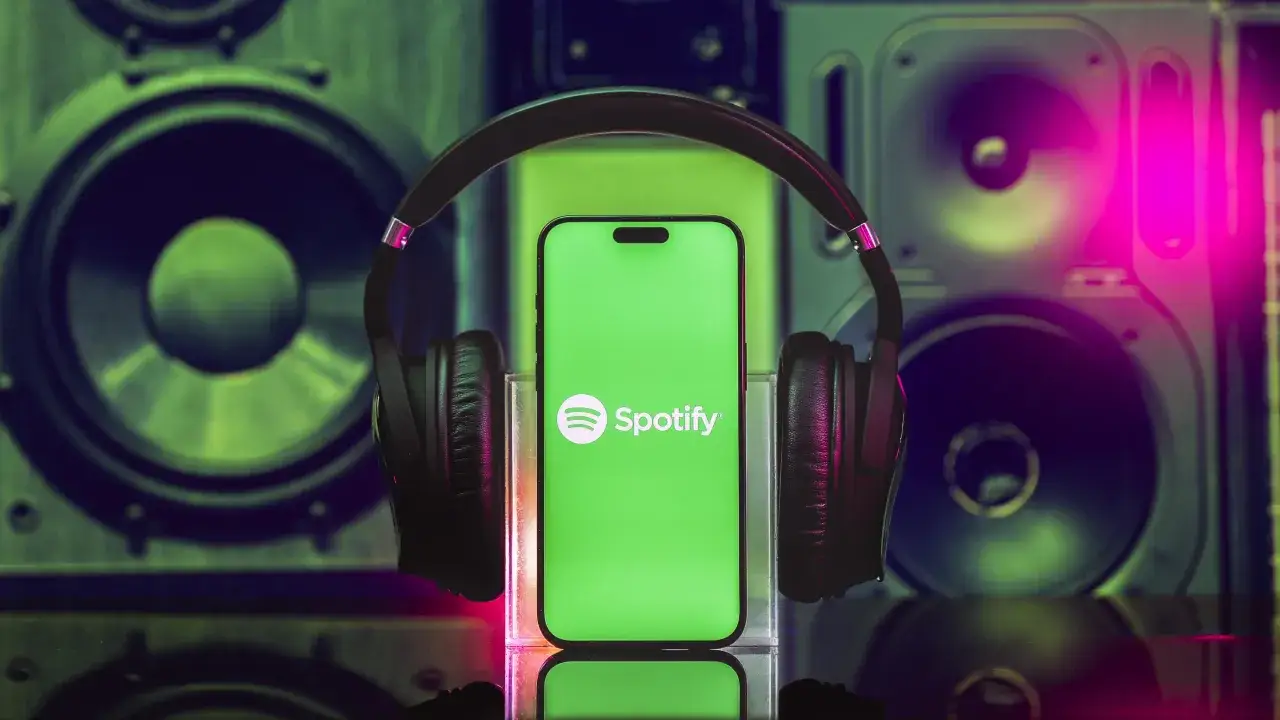Słuchawki i smartfon z logo Spotify na tle głośników. Ciesz się muzyką w jakości spotify lossless.