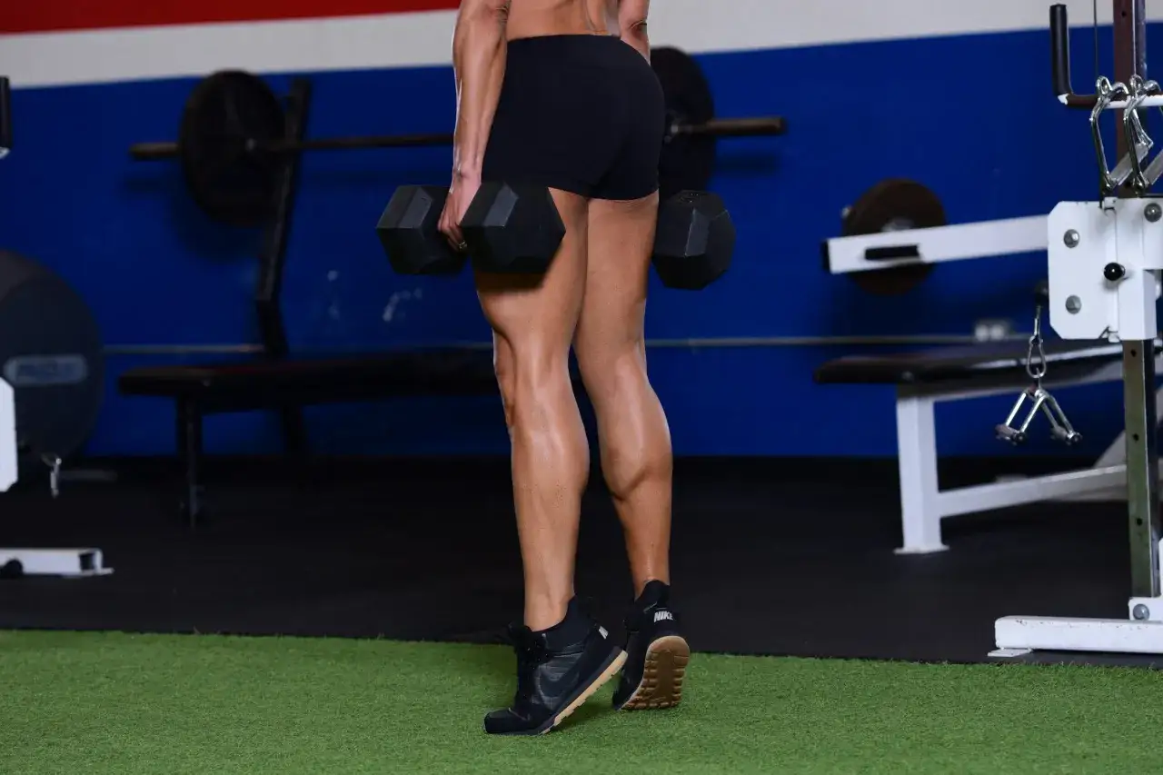 Femme musclée faisant un exercice mollet avec des haltères dans une salle de sport.