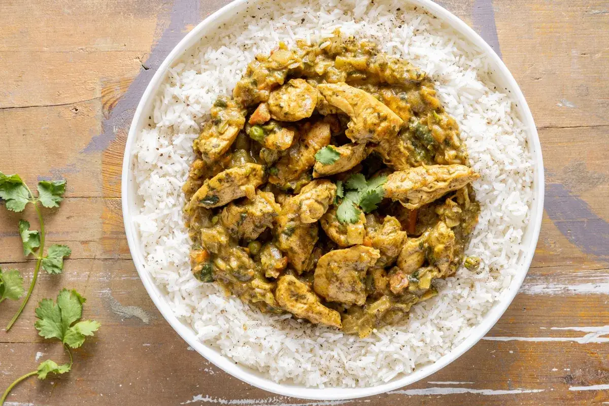 Straccetti di pollo al curry cremosi su un letto di riso basmati, guarniti con coriandolo fresco. Un piatto invitante e profumato.