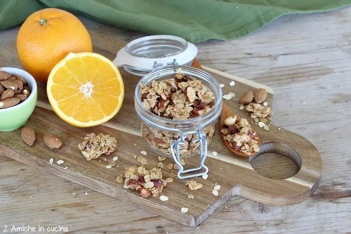 Granola fatta in casa con arancia e mandorle, servita in un barattolo di vetro e su un cucchiaio di legno.