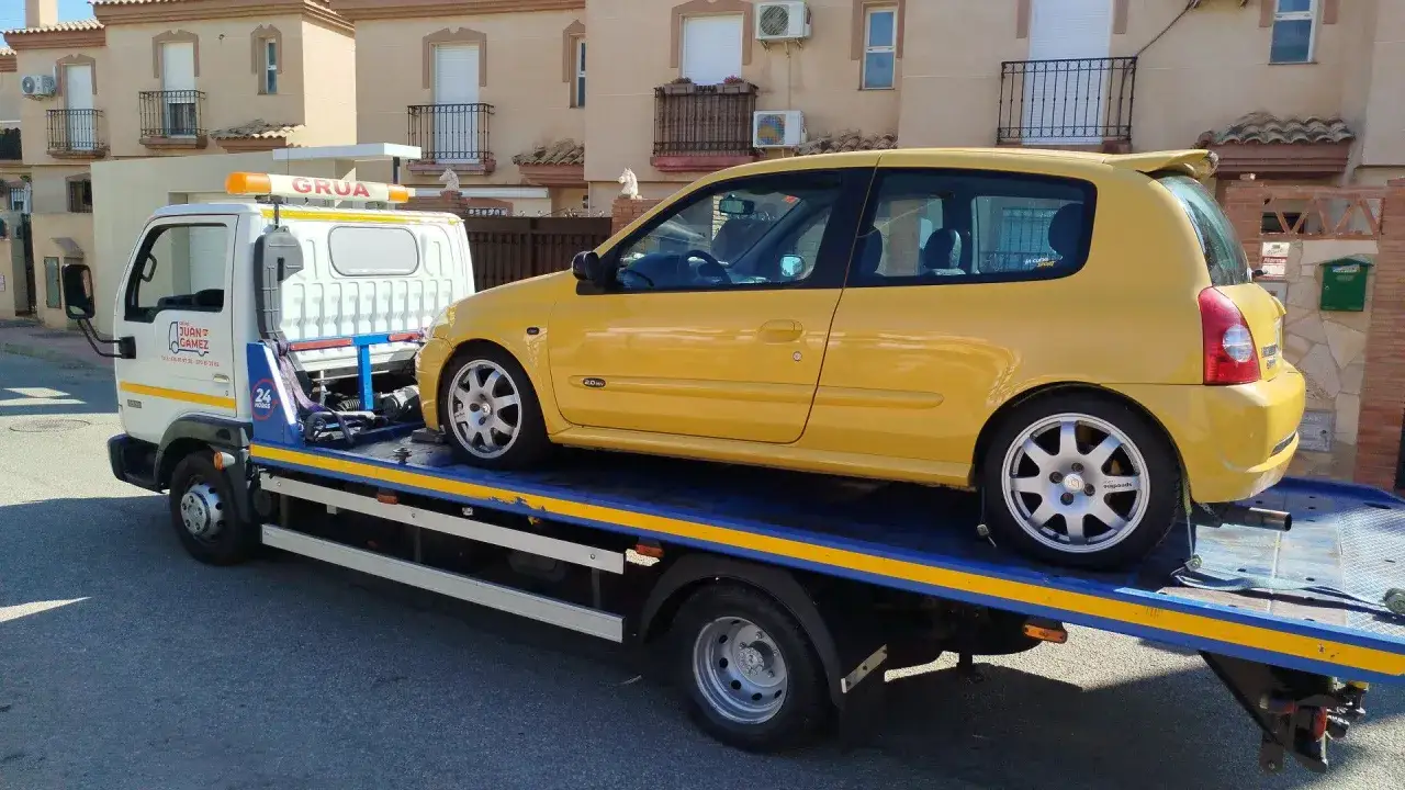 Grúa transportando un coche amarillo deportivo. El vehículo está sobre la plataforma de la grúa, listo para transportar.