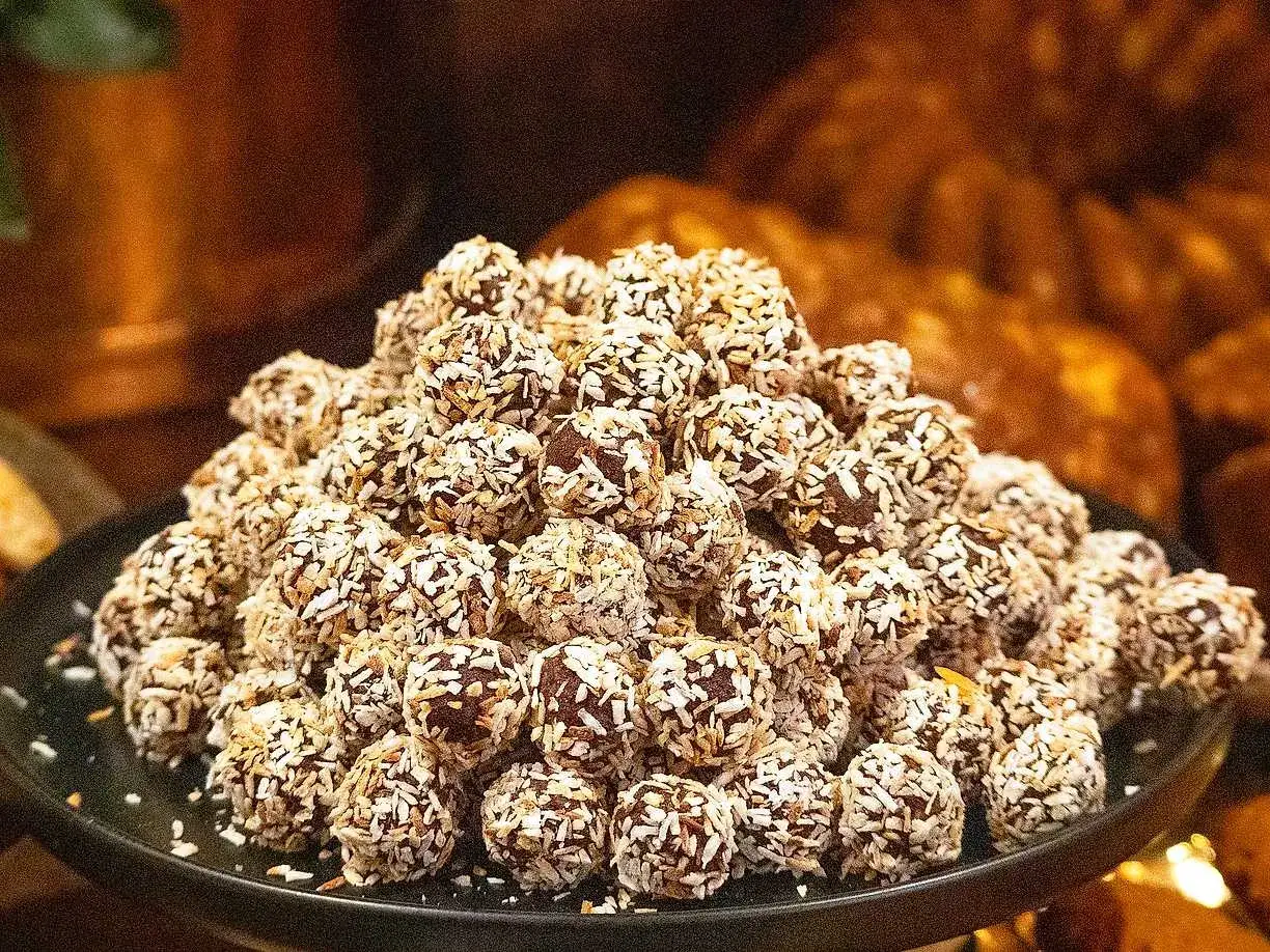 En hög med lyxiga chokladbollar, rullade i kokosflingor, ligger upplagda på en mörk tallrik.