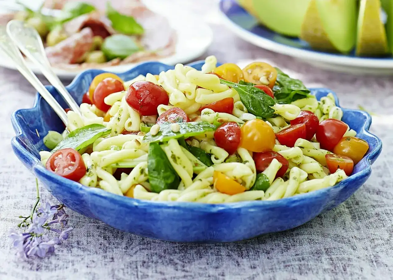 En blå skål fylld med godaste pastasalladen, full av körsbärstomater, spenat och pesto. Perfekt för en sommarlunch.