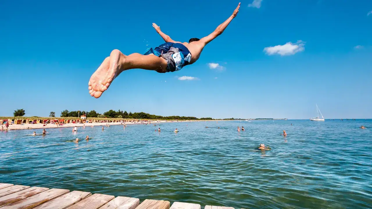 Ein Mann springt ins Wasser an einem sonnigen Tag an den Badeseen Schleswig-Holsteins. Viele Menschen genie&szlig;en das k&uuml;hle Nass.