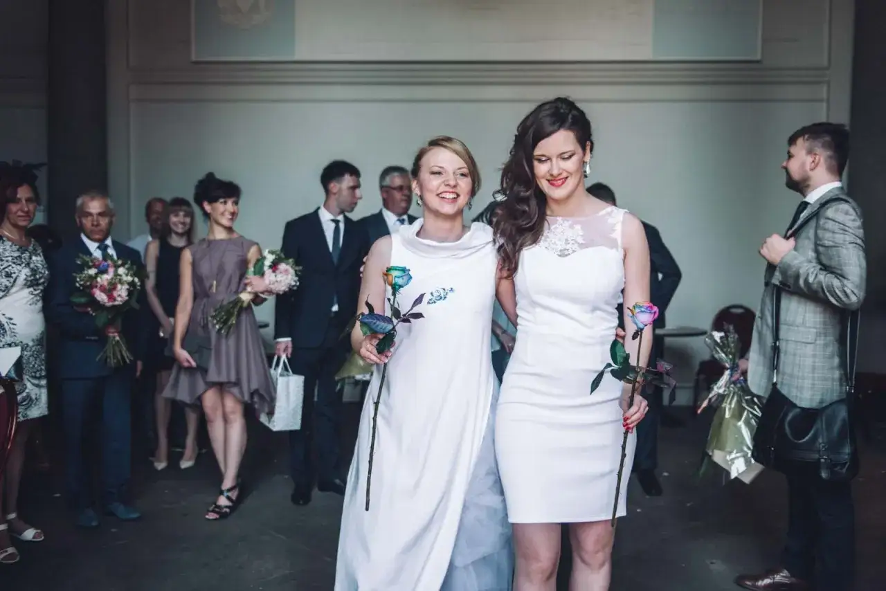 Dwie kobiety w białych sukniach, trzymające tęczowe róże, świętują swój ślub homoseksualny.