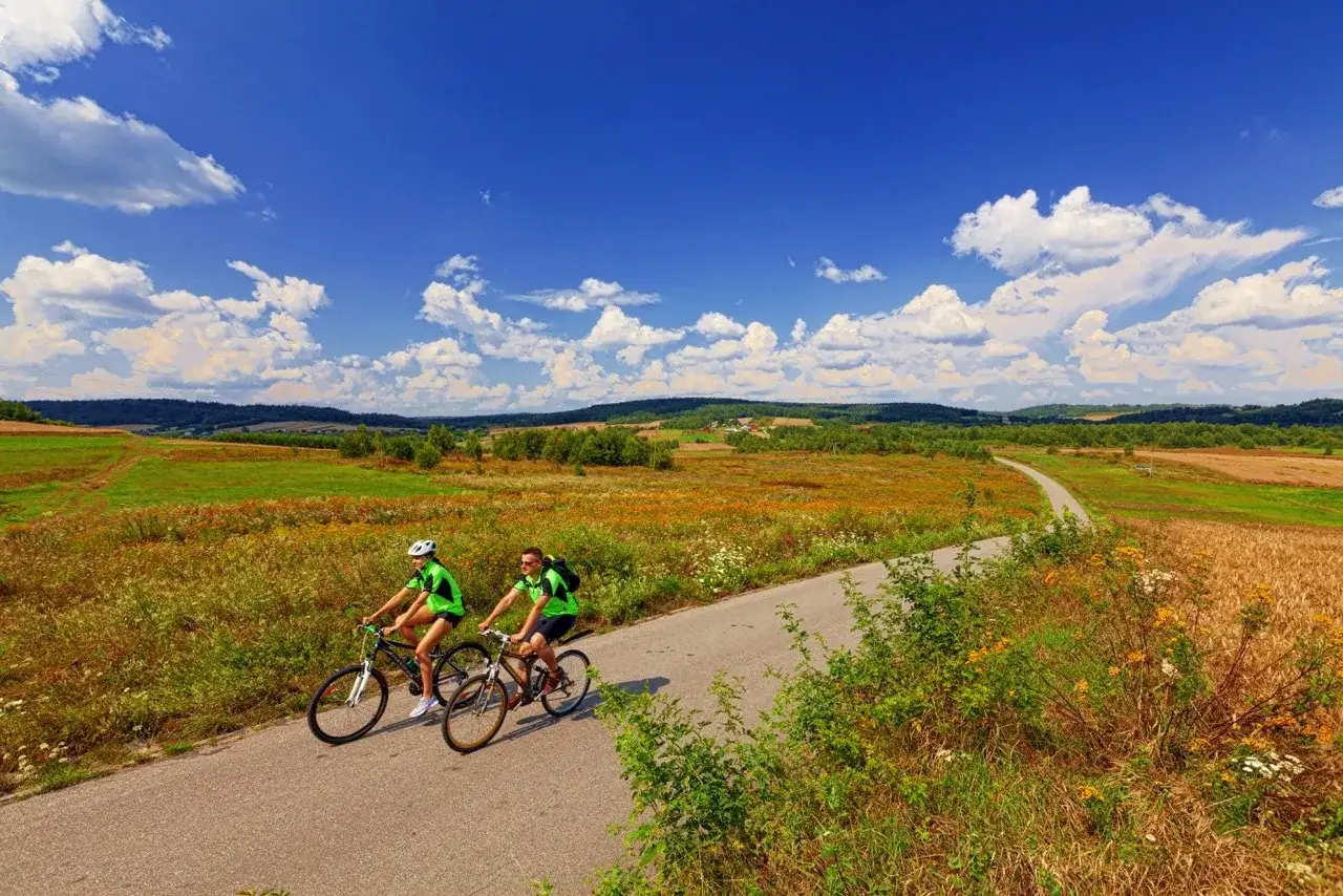 Dwie osoby w zielonych koszulkach pedałują po malowniczej trasie green velo świętokrzyskie, wśród pól i pagórków.