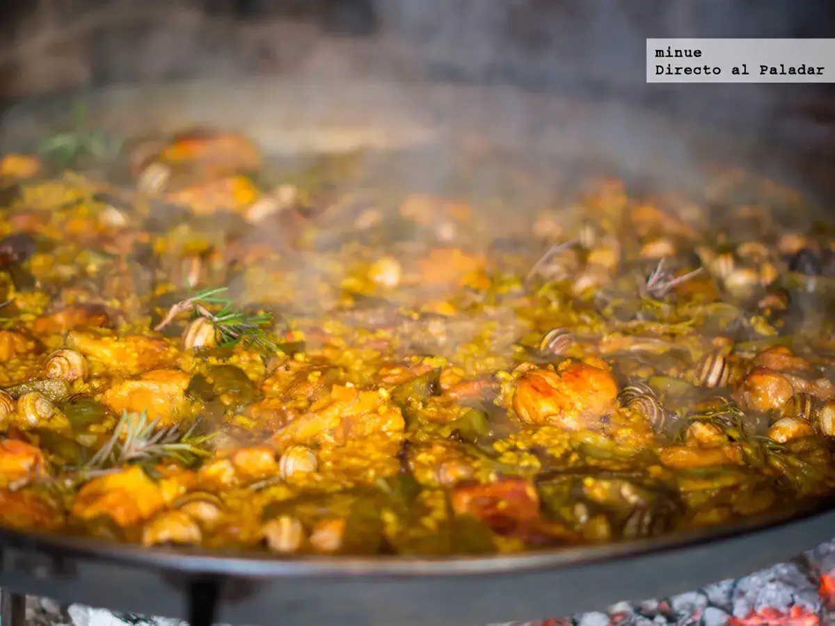 Paella valenciana con sus ingredientes: arroz, pollo, conejo, jud&iacute;as verdes y caracoles, cocin&aacute;ndose a fuego lento.