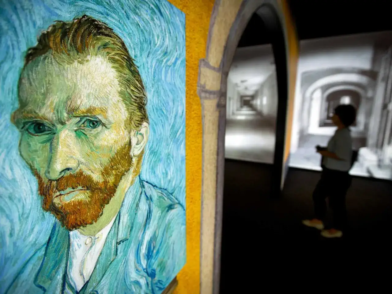 N&auml;rbild p&aring; Vincent van Goghs sj&auml;lvportr&auml;tt, med en bes&ouml;kare i bakgrunden som tittar p&aring; en projektion av en korridor. Kanske t&auml;nker bes&ouml;karen p&aring; Vincent van Goghs syskon.