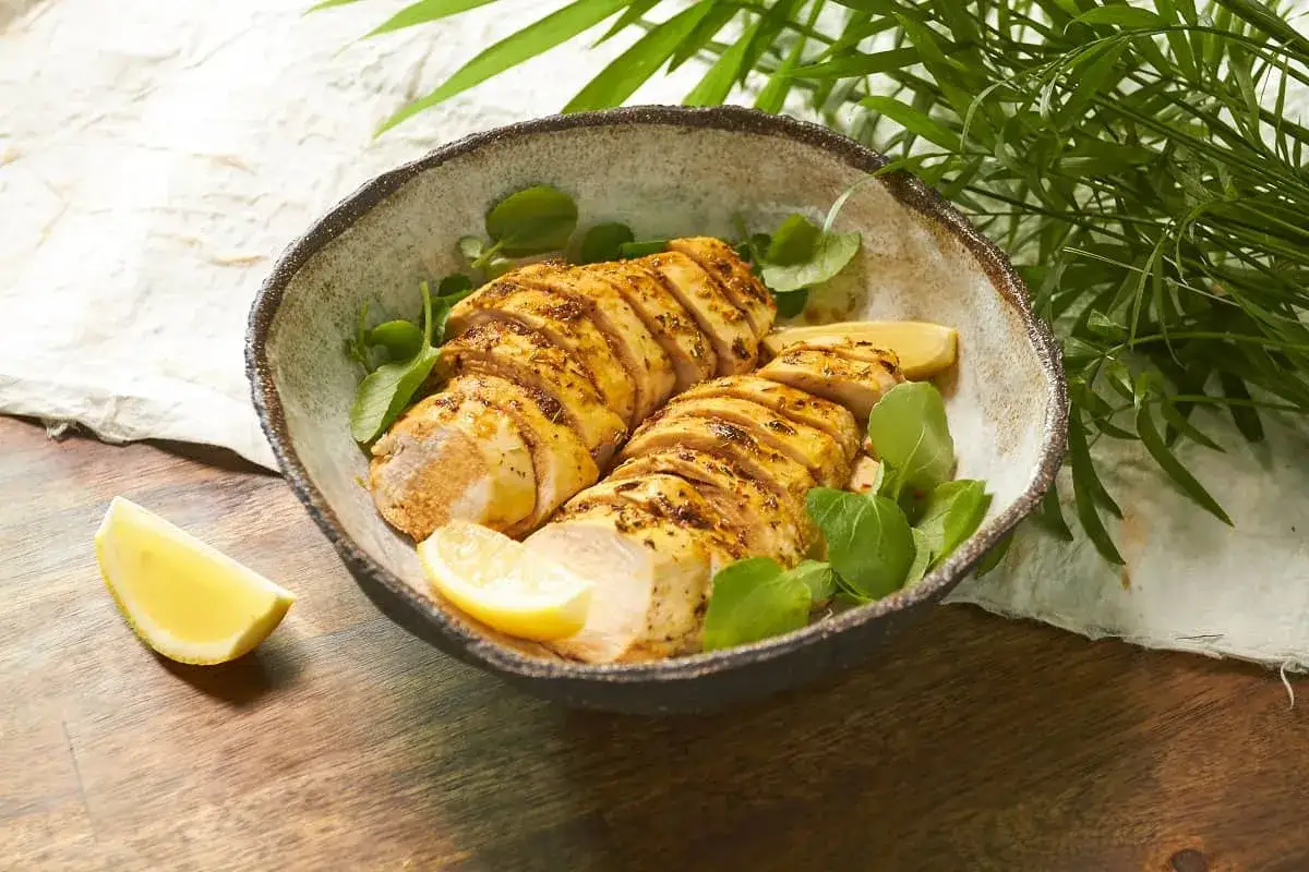 Sabroso pollo al lim&oacute;n cortado en rodajas, adornado con hojas verdes y gajos de lim&oacute;n en un cuenco r&uacute;stico.