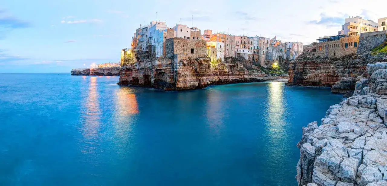 Polignano a Mare, un gioiello da scoprire tra le cose da vedere in Puglia. Case bianche aggrappate alle rocce a picco sul mare blu intenso.
