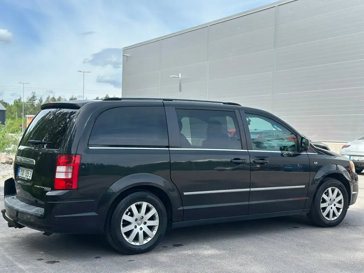 Svart Chrysler Voyager parkerad framf&ouml;r en gr&aring; byggnad. Bilen har tonade rutor och takr&auml;cken.