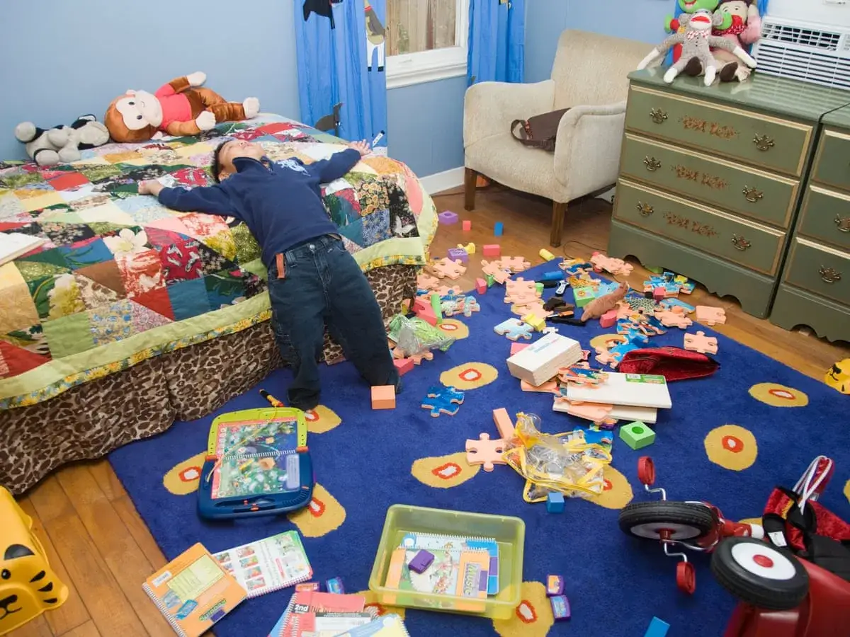 Un ni&ntilde;o yace en una cama en una habitaci&oacute;n desordenada llena de juguetes esparcidos por el suelo.