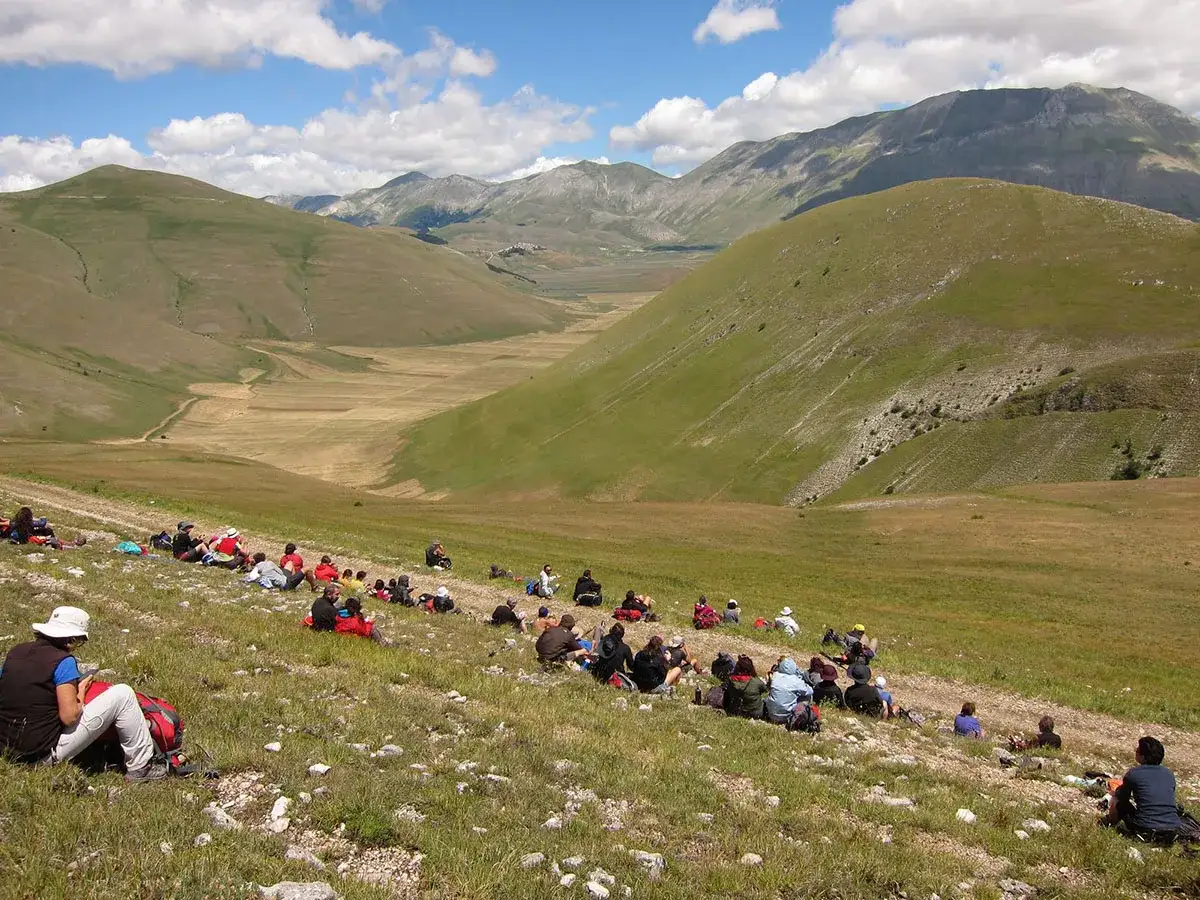 Un gruppo di escursionisti riposa su un prato fiorito, godendosi il panorama mozzafiato del cammino delle terre mutate.
