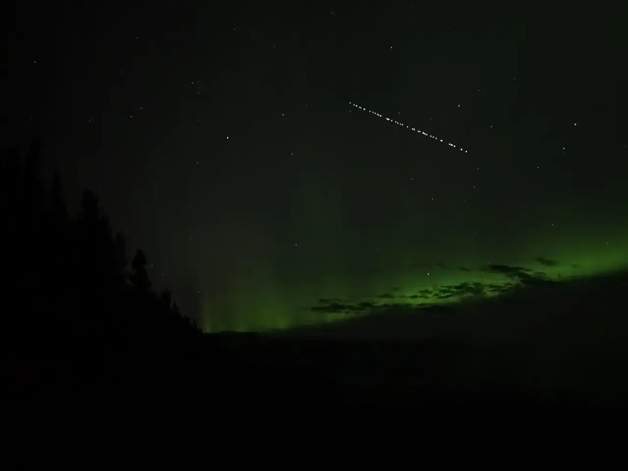 Nocne niebo z zorzą polarną i smugą satelitów Starlink.