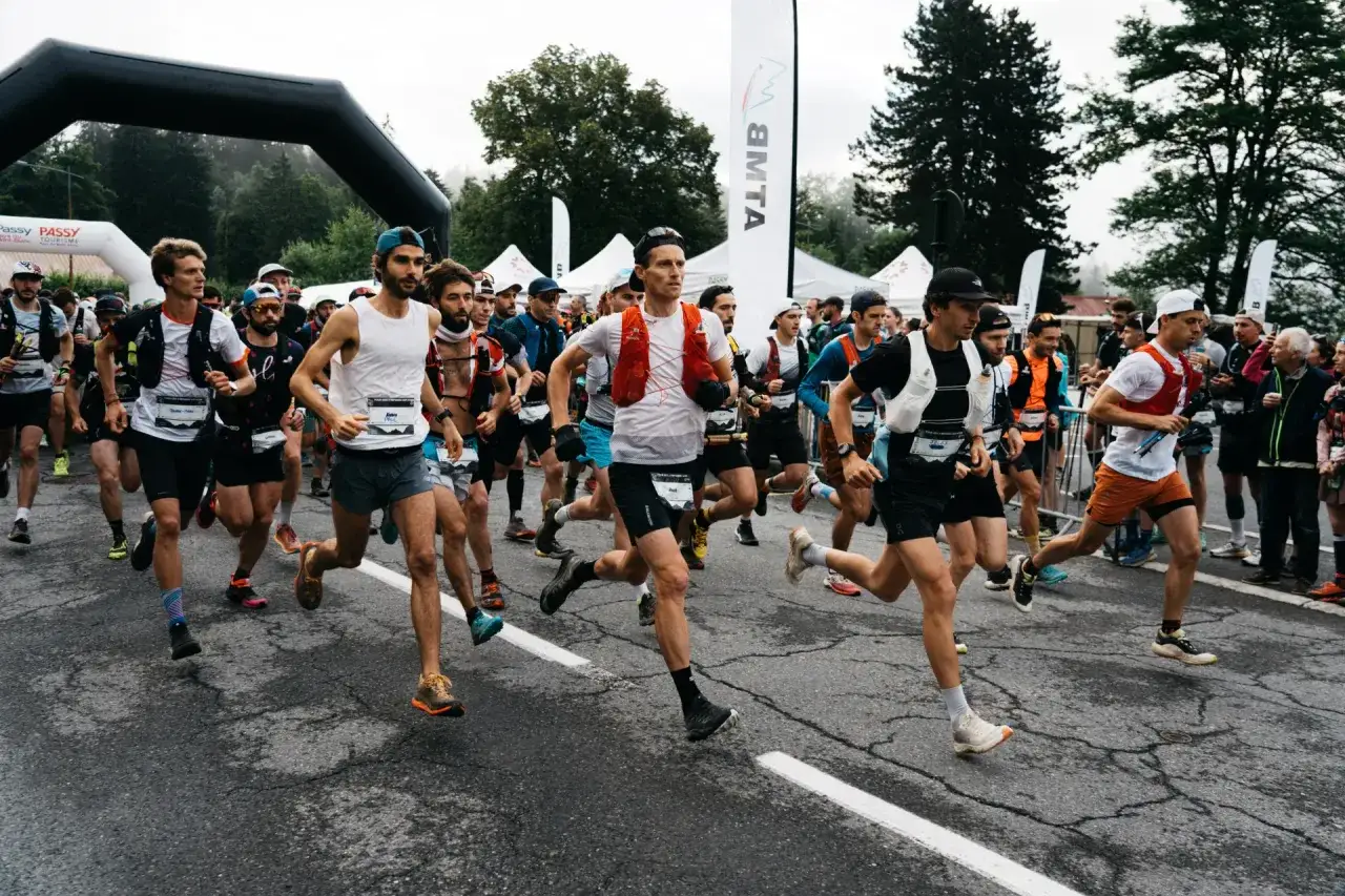 Des coureurs s'élancent au départ du trail des Fiz, sous une arche noire, prêts à affronter le parcours.