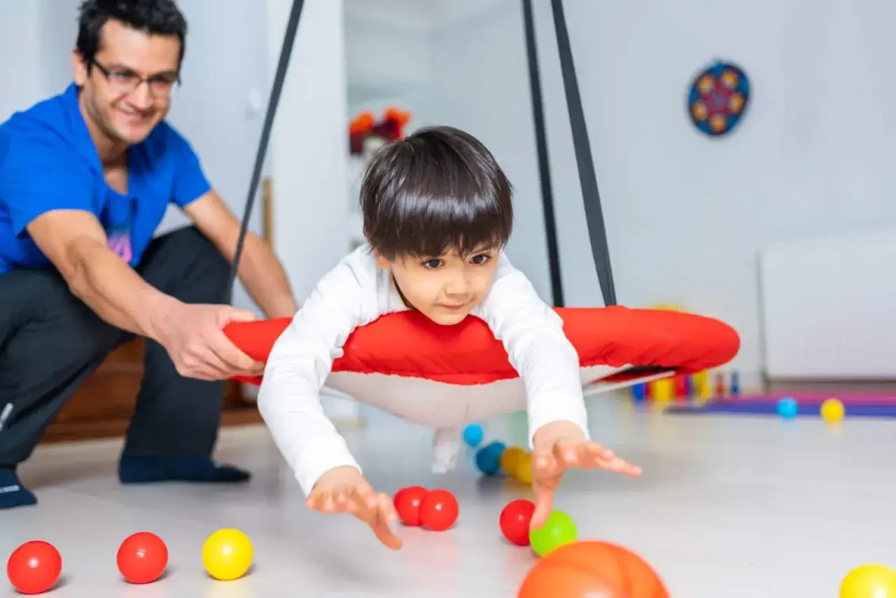 Chłopiec z autyzmem ćwiczy na huśtawce terapeutycznej. Terapia sensoryczna wspiera rozwój.