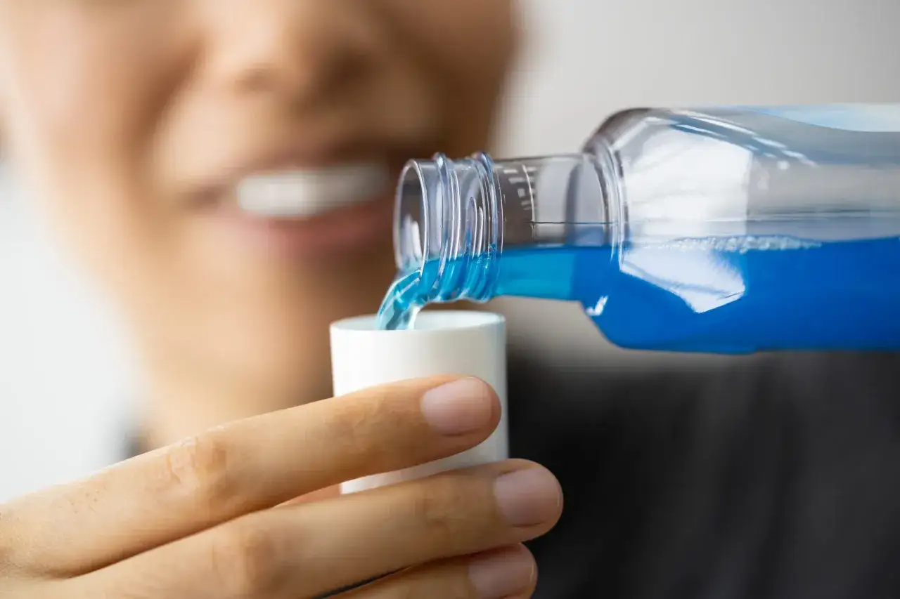 Una persona versa collutorio blu in un tappo bianco. Ricorda che il collutorio va risciacquato.