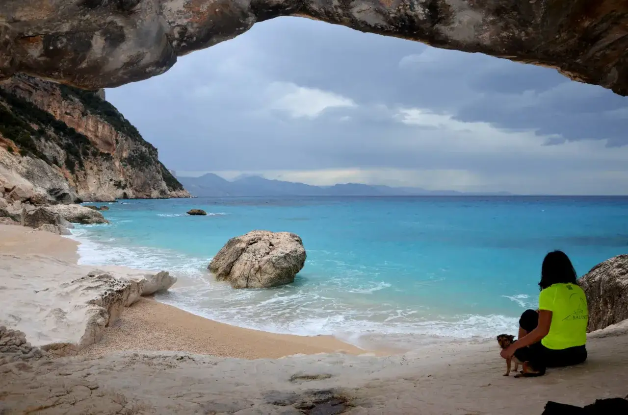 Vista dalla grotta di Cala Goloritz&egrave;, raggiungibile con un percorso a piedi. Una donna con un cane ammira il mare turchese.