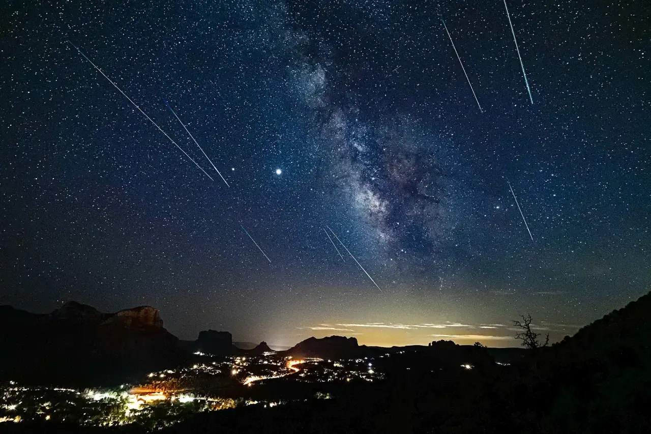 Nocne niebo nad miastem rozświetlają spadające gwiazdy, tworząc magiczny widok perseidów.