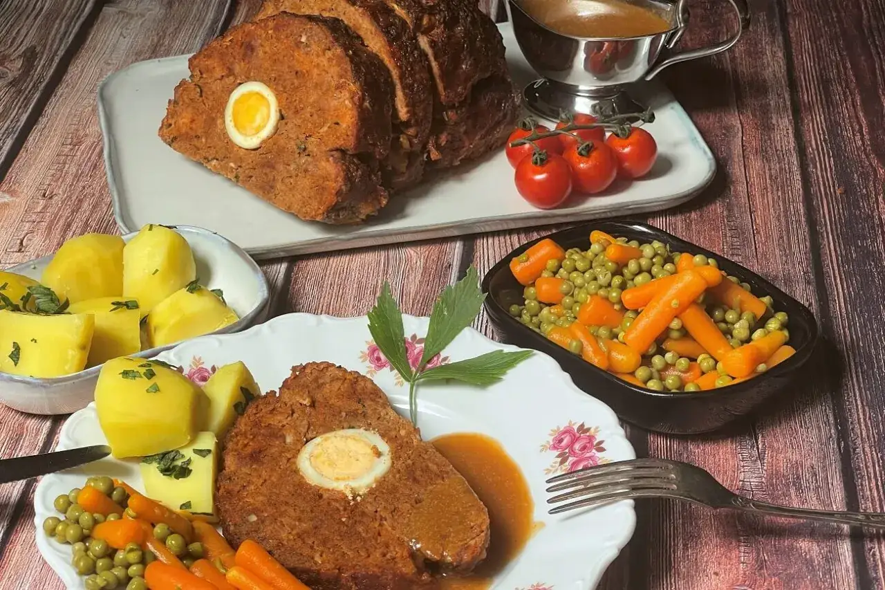 Ein herzhafter falscher Hase mit gekochtem Ei im Inneren, serviert mit Kartoffeln, Erbsen, Karotten und Bratensoße.