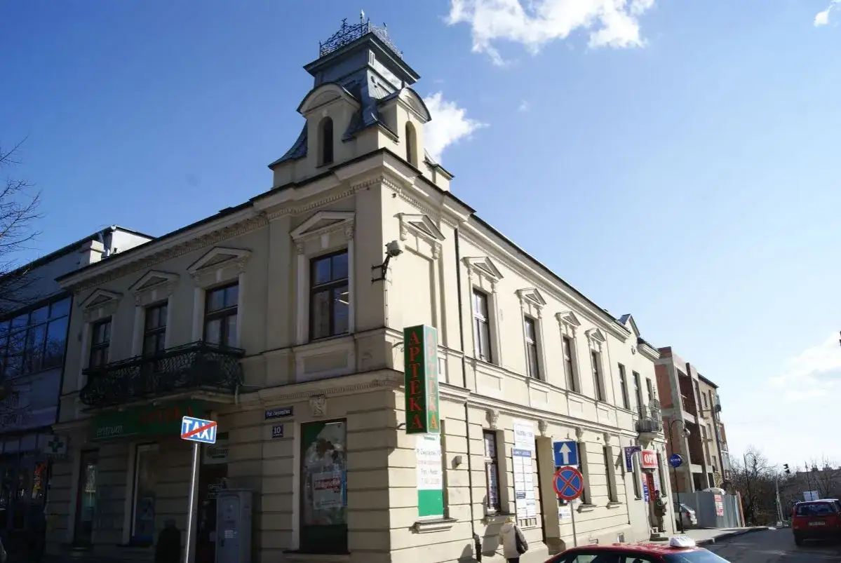 Kamienica na Busko Zdr&oacute;j Rynek, z apteką i sklepami na parterze. Słoneczny dzień, błękitne niebo z chmurami.