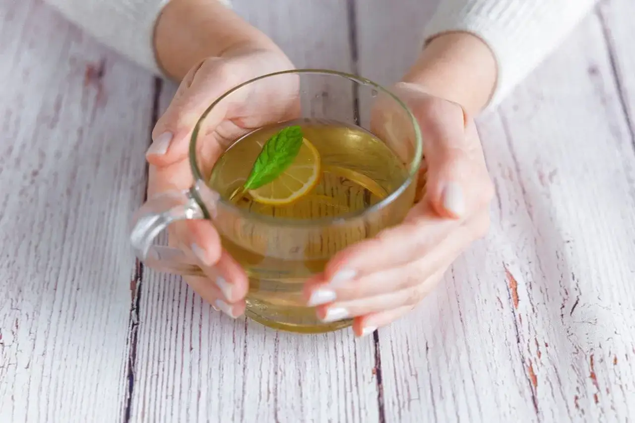 Hände halten eine Tasse mit Pfefferminztee und Zitrone. Ein erfrischender Drink, der beim Abnehmen helfen kann.