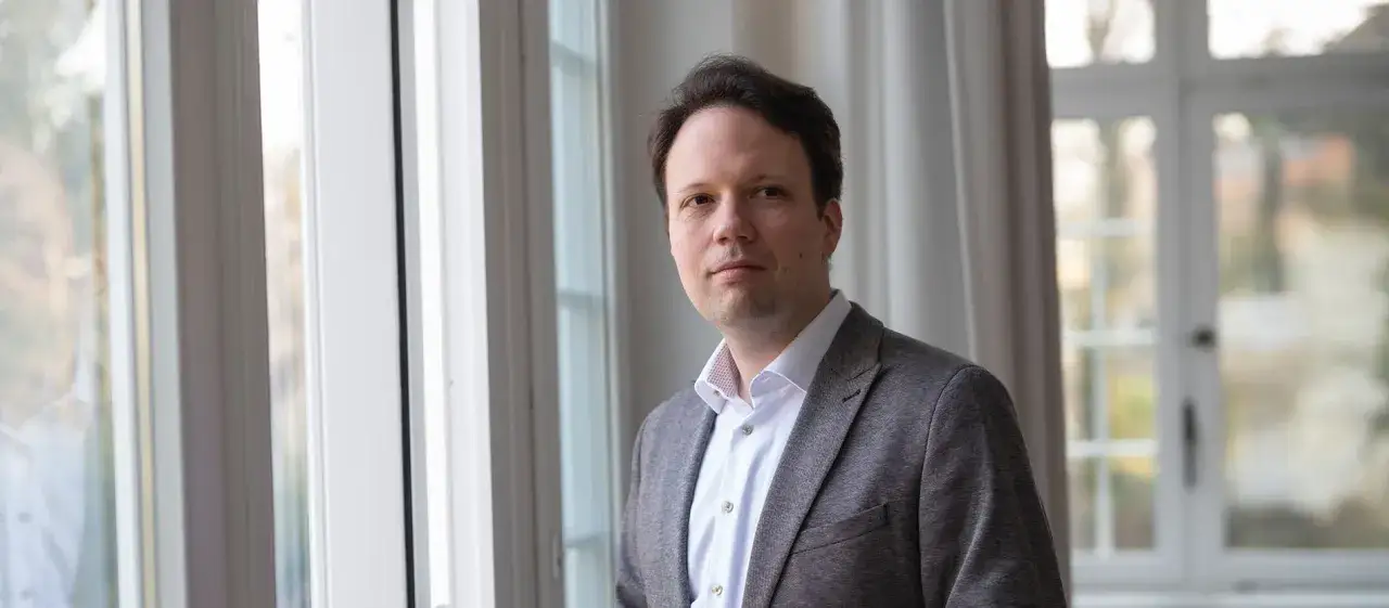 Michael Seewald blickt nachdenklich in die Kamera, im Hintergrund ein Fenster mit Vorhängen.