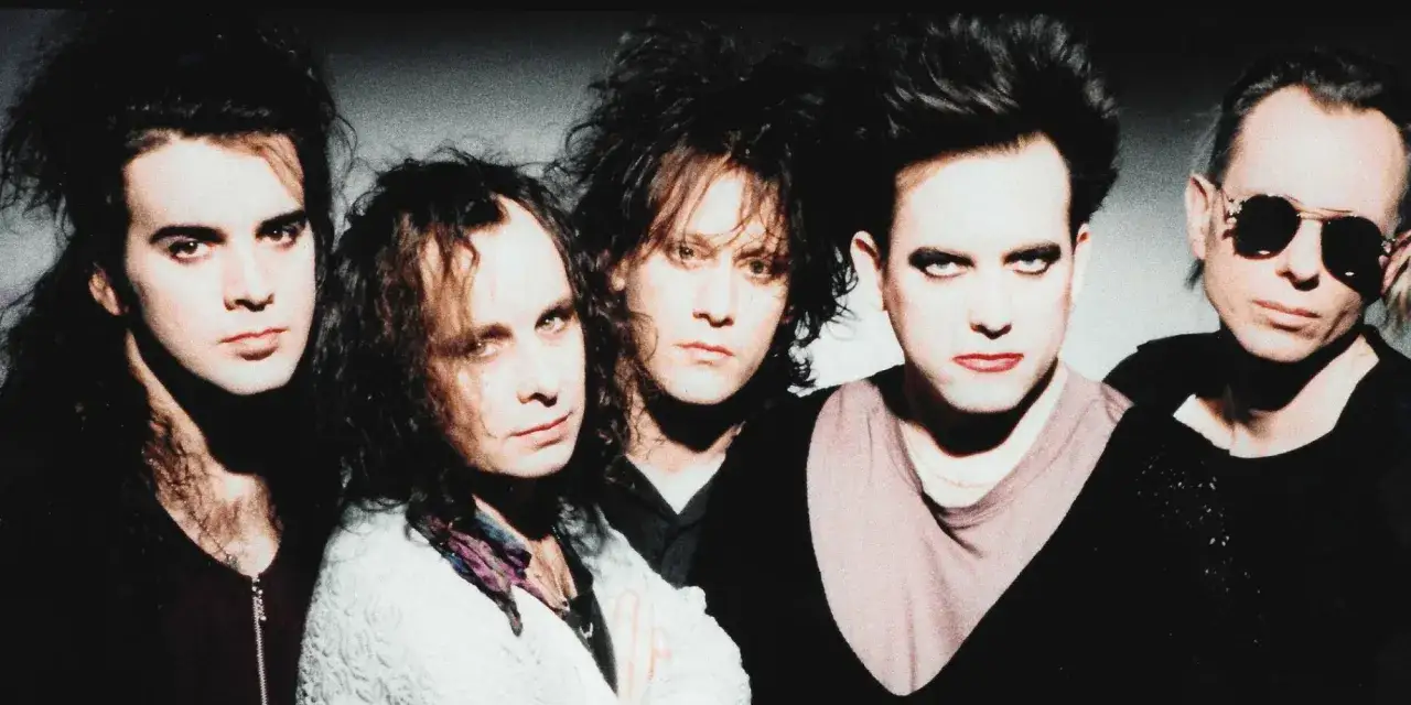 Członkowie The Cure w charakterystycznych fryzurach i makijażu, pozujący do zdjęcia.