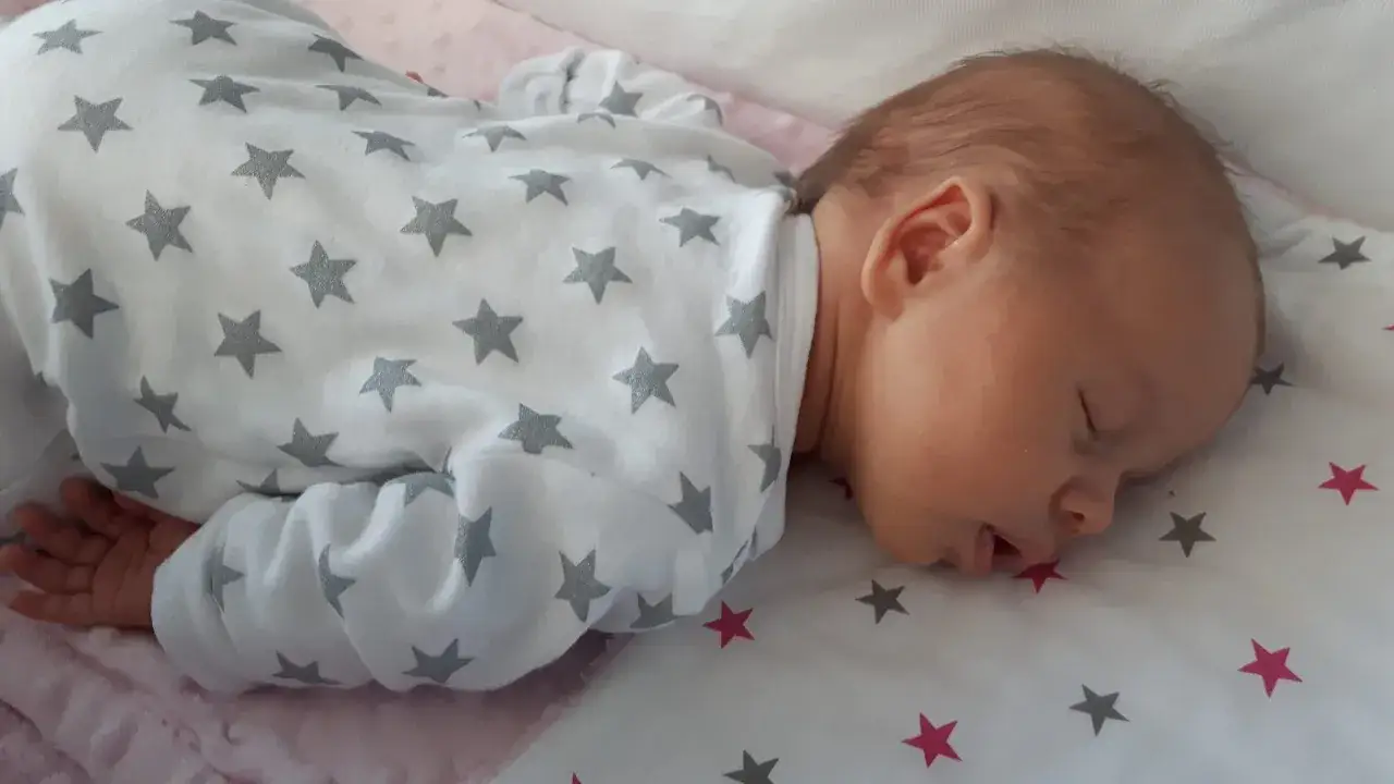 Słodki sen maluszka w piżamce w gwiazdki. Niemowlę śpi z otwartą buzią, marząc o gwiazdkach.