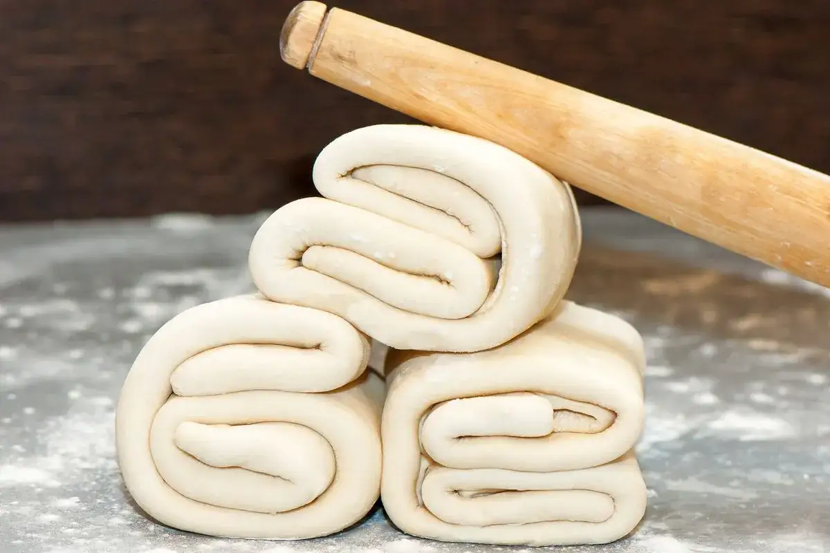 Rotolo da cucina appoggiato su pasta sfoglia piegata, pronta per una ricetta pasta sfoglia veloce.