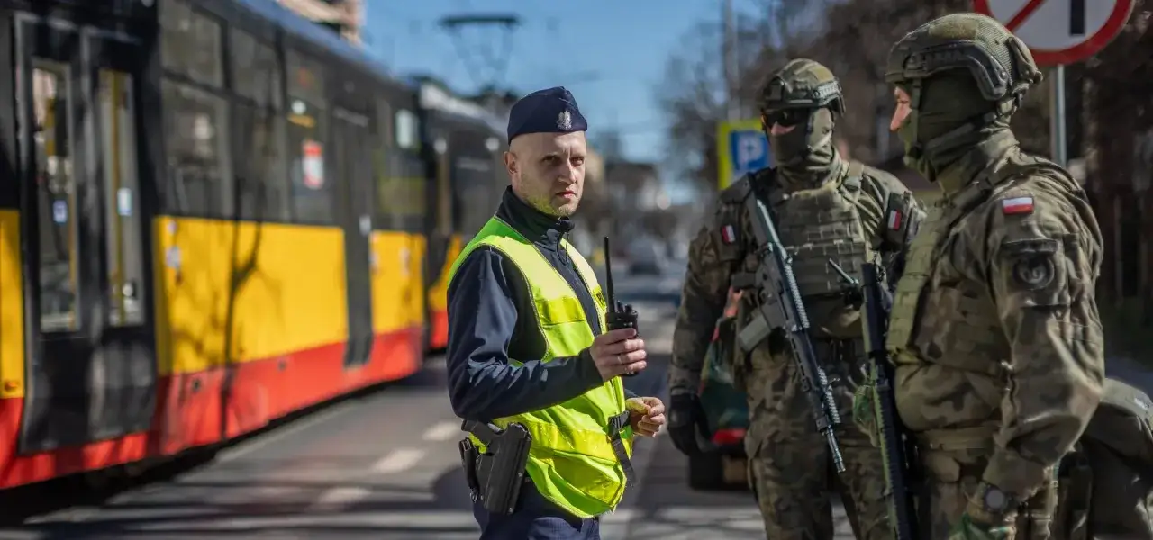 Policjant i żołnierze w pełnym rynsztunku, gotowi do działania. **Stopień alarmowy bravo** podnosi czujność.