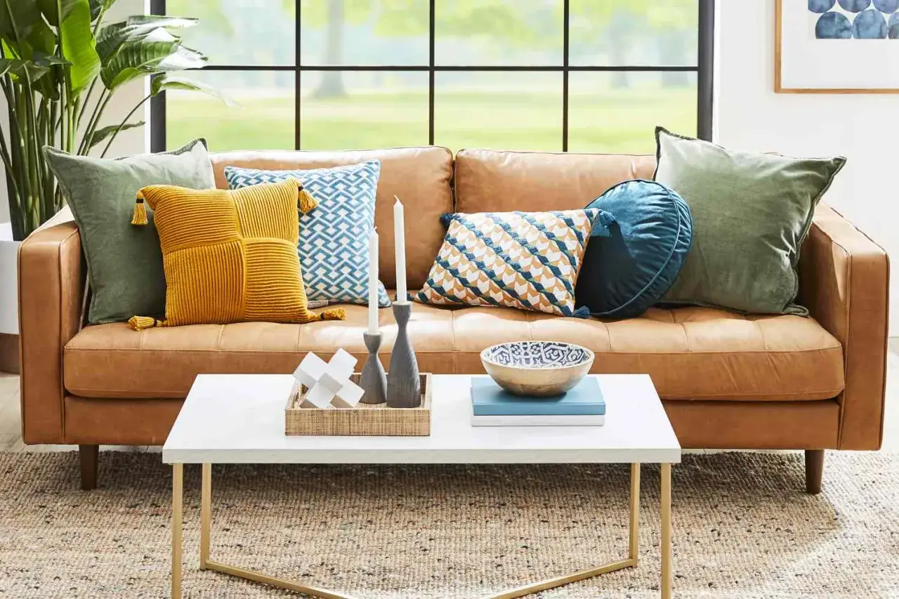 Learn how to style pillows on a couch with this inviting arrangement: green, mustard, and patterned pillows create a cozy, textured look on a tan leather sofa.