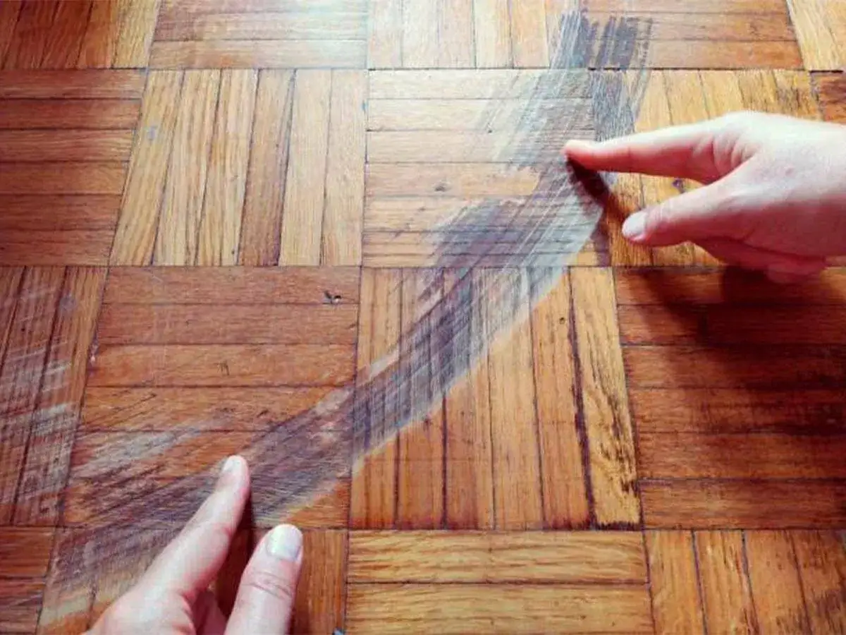 Manos se&ntilde;alan un &aacute;rea da&ntilde;ada en un suelo de parquet, mostrando el resultado de un acuchillado de parquet mal ejecutado.