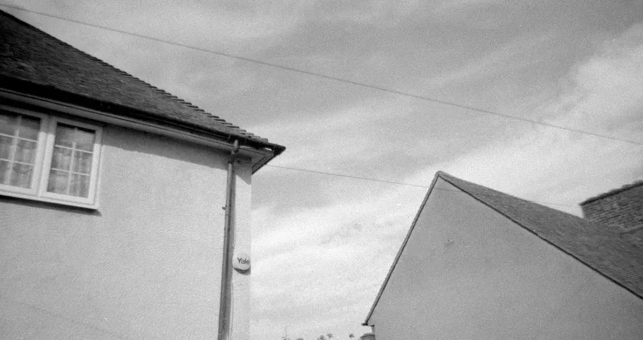 A black and white image, likely shot on Kentmere 400 film, shows the angled roofs of two houses against a cloudy sky.