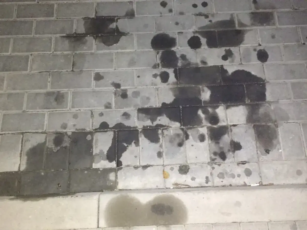 Plama pod samochodem z przodu, ciemne plamy oleju na szarej kostce brukowej.