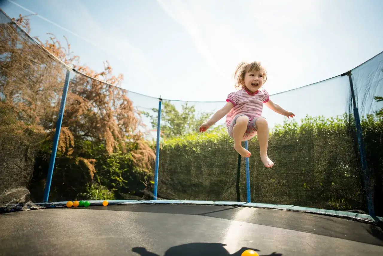 Ein fröhliches kleines Mädchen springt hoch auf einem Trampolin. Die Frage