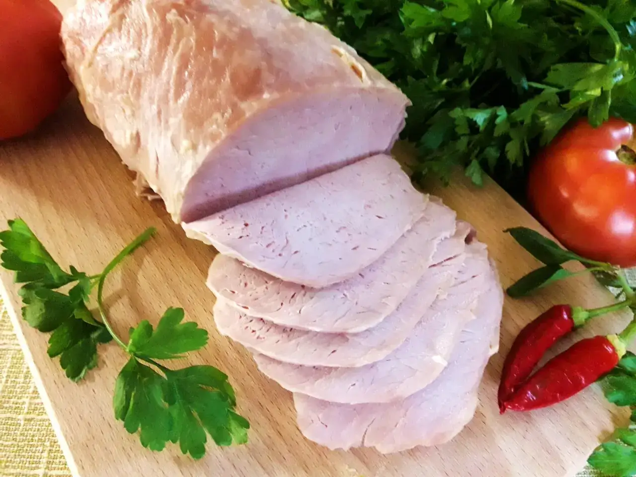 Schab gotowany 2 razy po 5 minut, pokrojony w plastry, z pomidorami, papryczkami chili i natką pietruszki na desce.