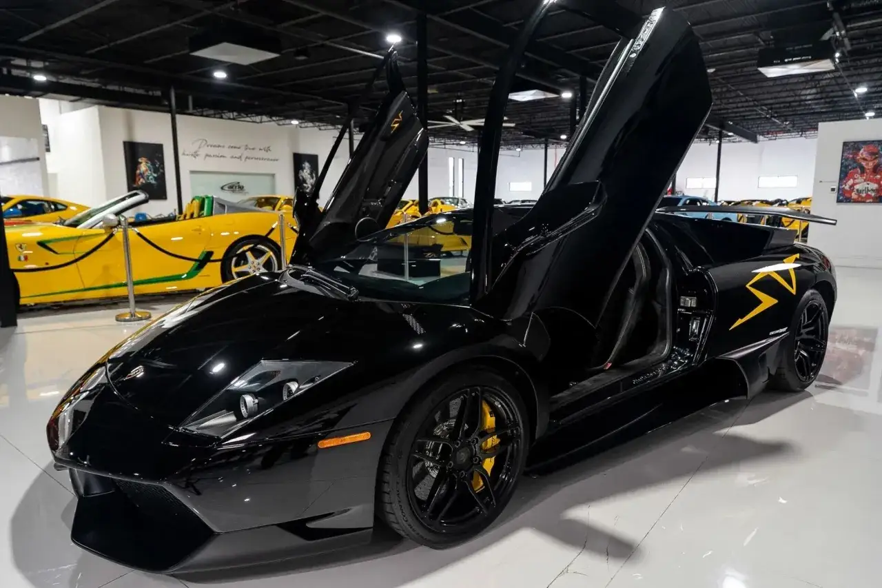 Czarny Lamborghini Murcielago z otwartymi drzwiami, z żółtymi akcentami na karoserii, stoi w salonie samochodowym obok żółtego Ferrari.