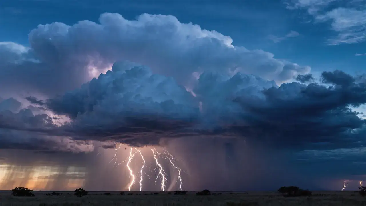 Dramatic lightning photography captures multiple bright bolts striking the plains under a turbulent, dark blue sky filled with massive storm clouds.