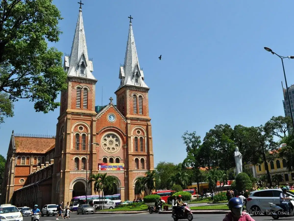 Katedra Notre Dame w Sajgonie, dawna nazwa miasta Ho Chi Minh, z ruchem ulicznym i palmami.