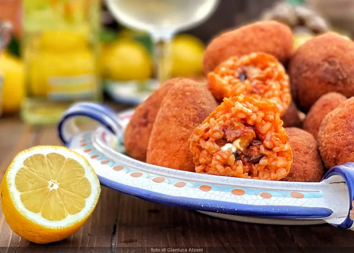 En tallrik med siciliansk mat: friterade arancini med ris och fyllning, samt en halv citron.
