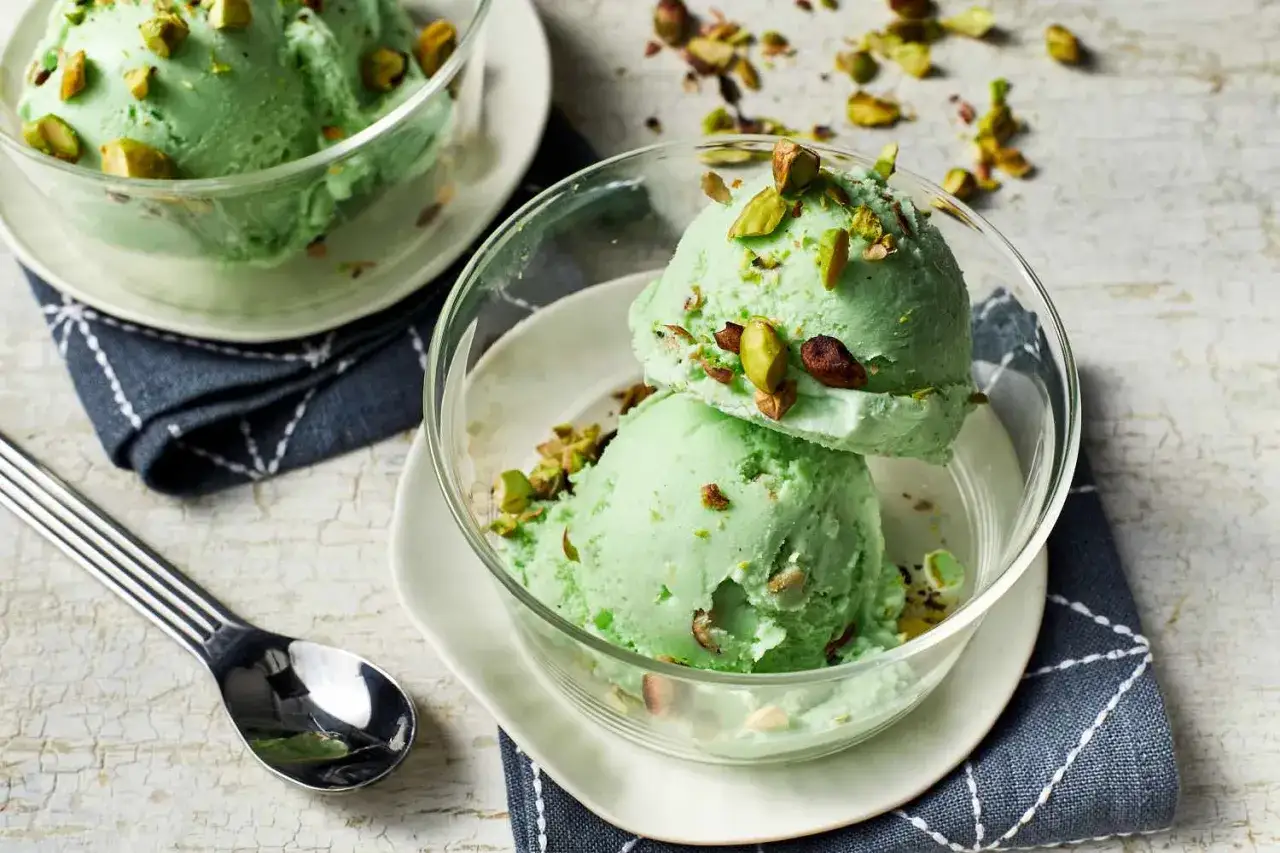 Dos bolas de cremoso helado de pistacho adornadas con trozos de pistacho en un cuenco de cristal.
