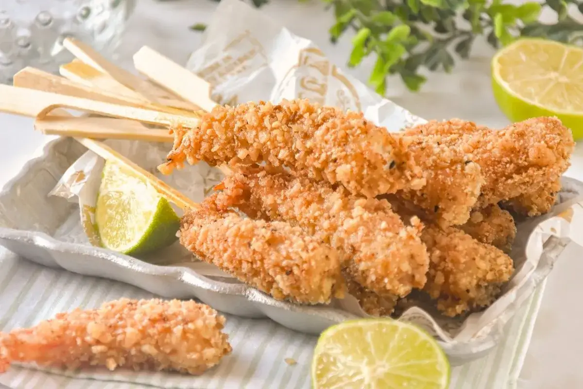 Crujientes gambas a la gabardina en brochetas, servidas con gajos de lima.