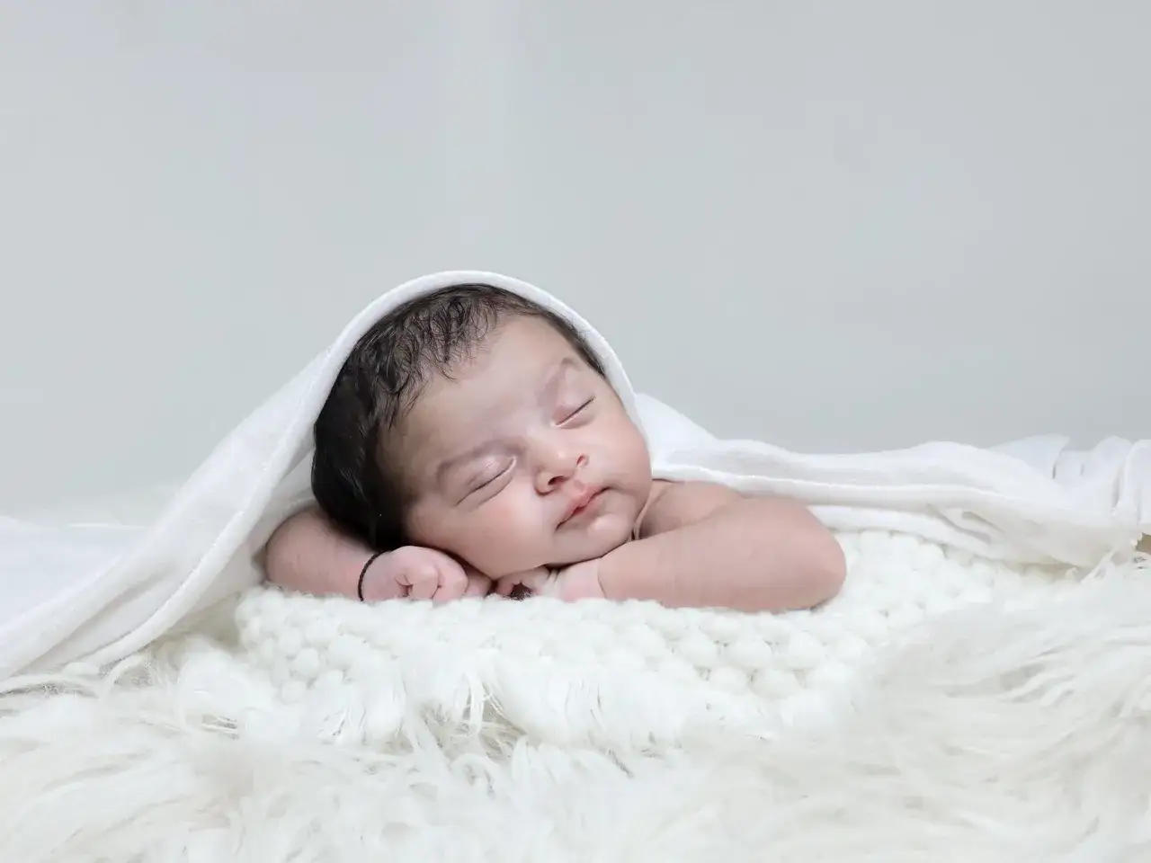 Bebé durmiendo sobre manta blanca. Si te preguntas como saber si un bebe tiene sindrome de down, consulta a un profesional.