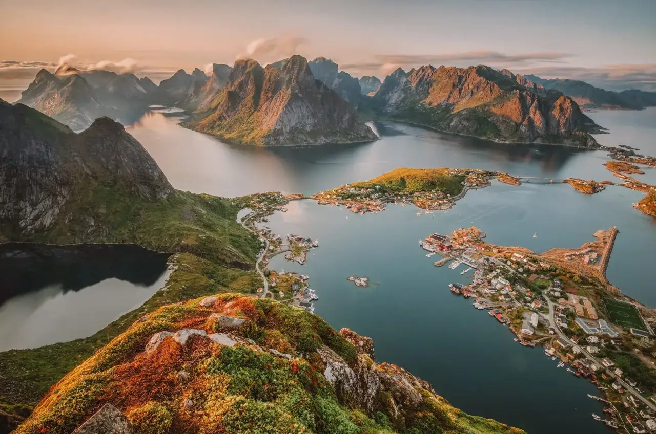 Vacker vy över en norsk kustby med röda hus och båtar, omgiven av dramatiska berg och fjordar. En av många norge sevärdheter.