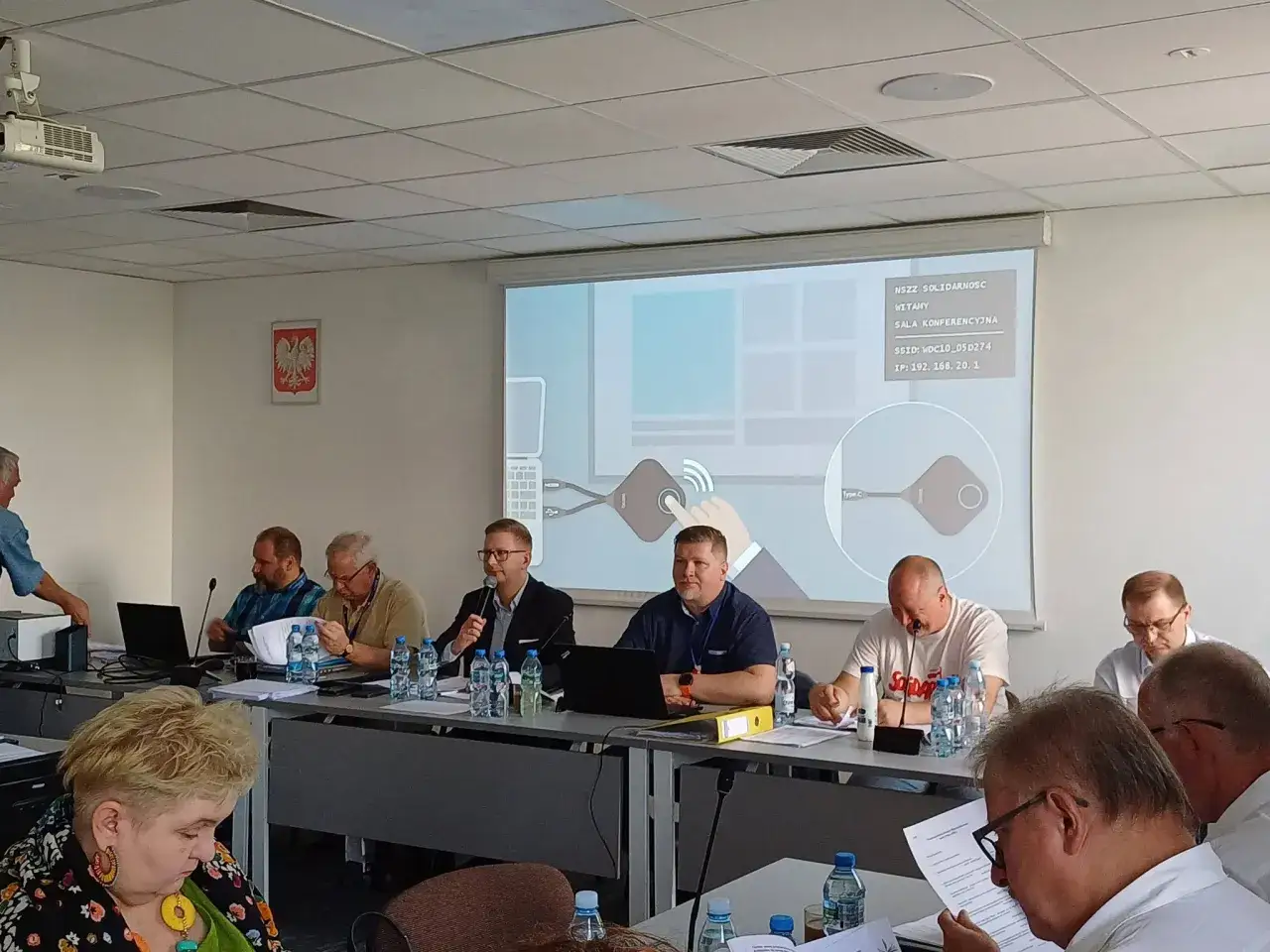 Obrady zarządu w sali konferencyjnej. Na ekranie logo 
