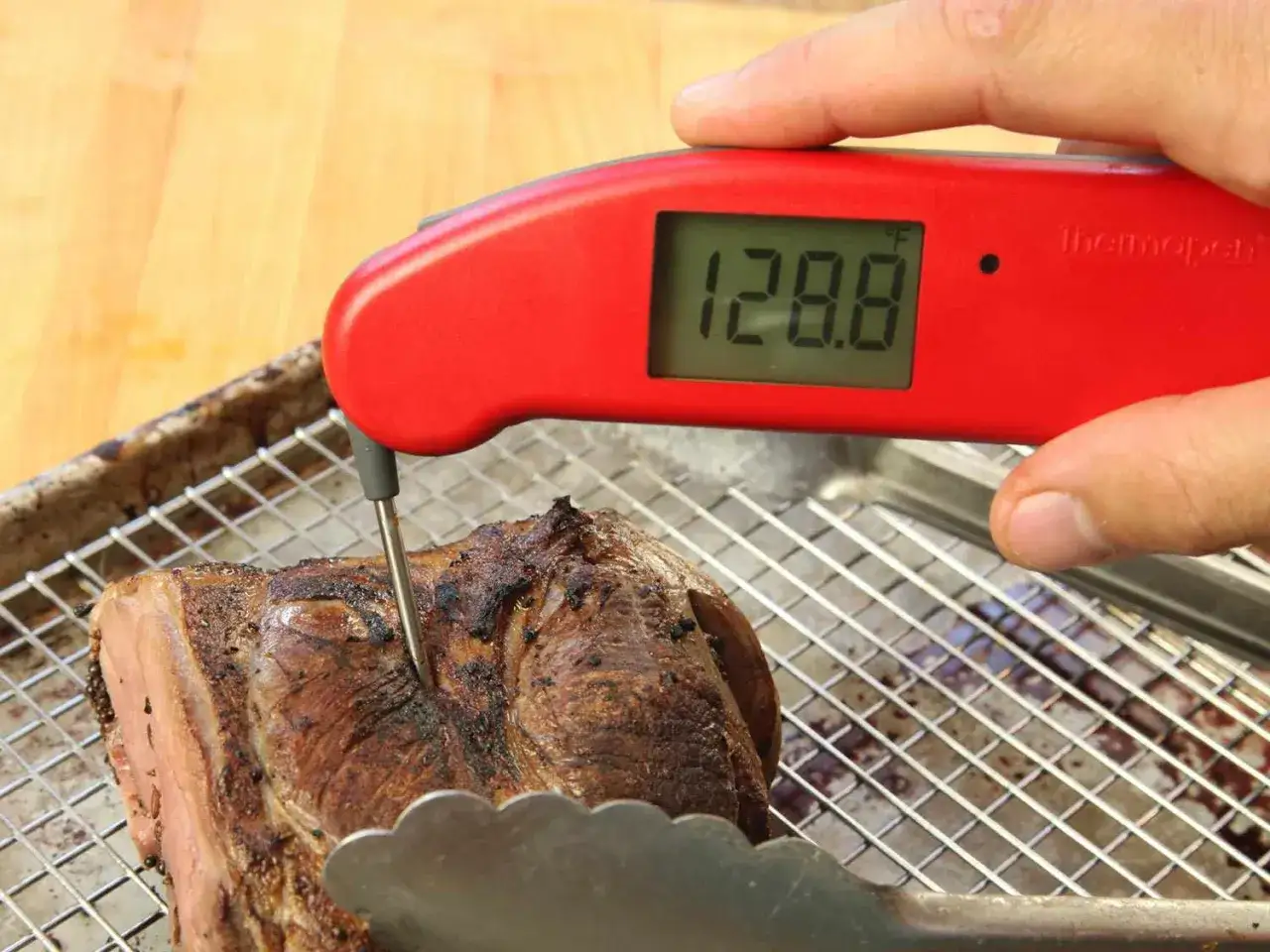 Röd digital termometer mäter köttets innertemperatur till 128.8°F, perfekt för medium rare.
